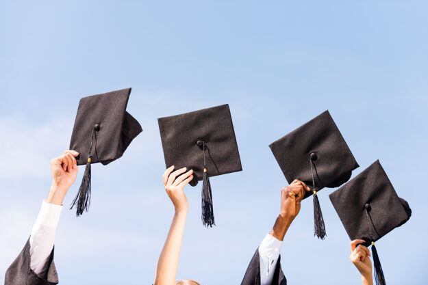 Finally graduated! Close-up of four hands holding mortar boards